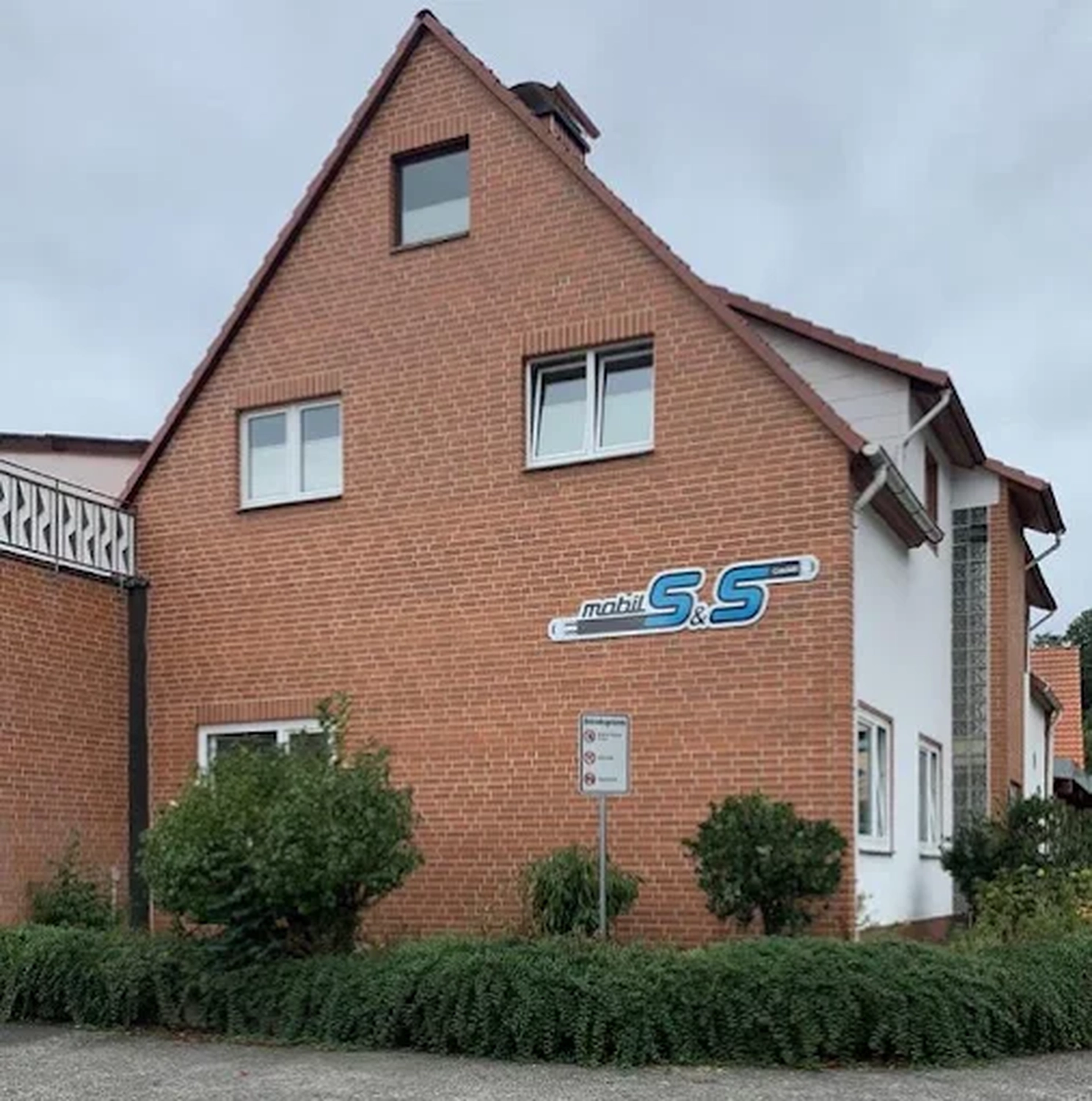mobil s&s GmbH - Maschinenbau - Zweistöckiges rotes Backsteinhaus mit einem markanten blau-weißen Logo von „Mobil S&S“ an der Seite.